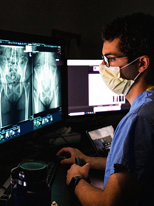 Resident wearing a mask examining a musculoskeletal scan in a dark reading room at MIR in St. Louis, Missouri