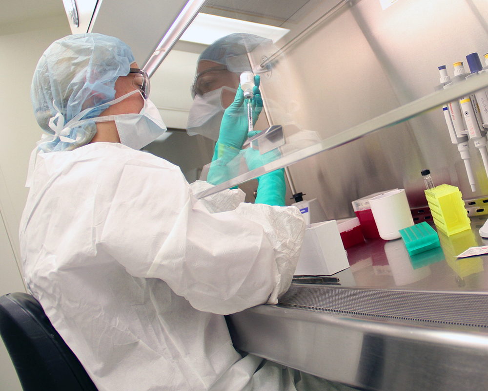 A molecular imaging researcher in the Precision Radiotheranostics Translation Center extracts fluid from a vial with a syringe while sitting at a fume hood in a laboratory.
