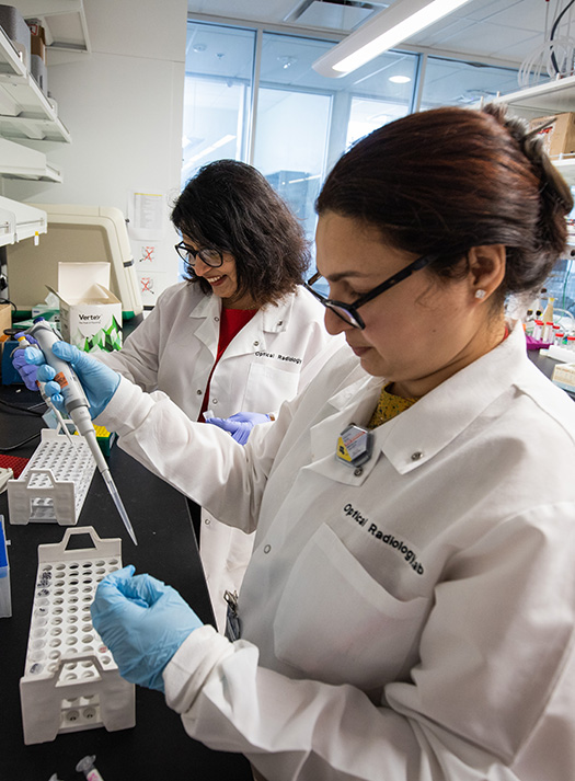 Two researchers from the Biophotonics Research Center use pipettes while working in a lab.
