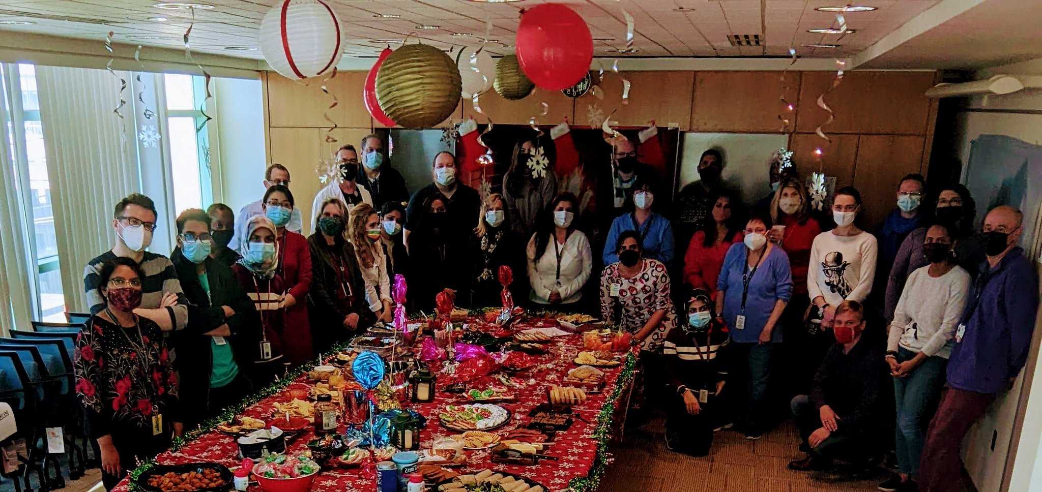 Around 30 lab members pose wearing masks, with some wearing green reindeer antlers, Santa Claus hats, or holiday outfits.