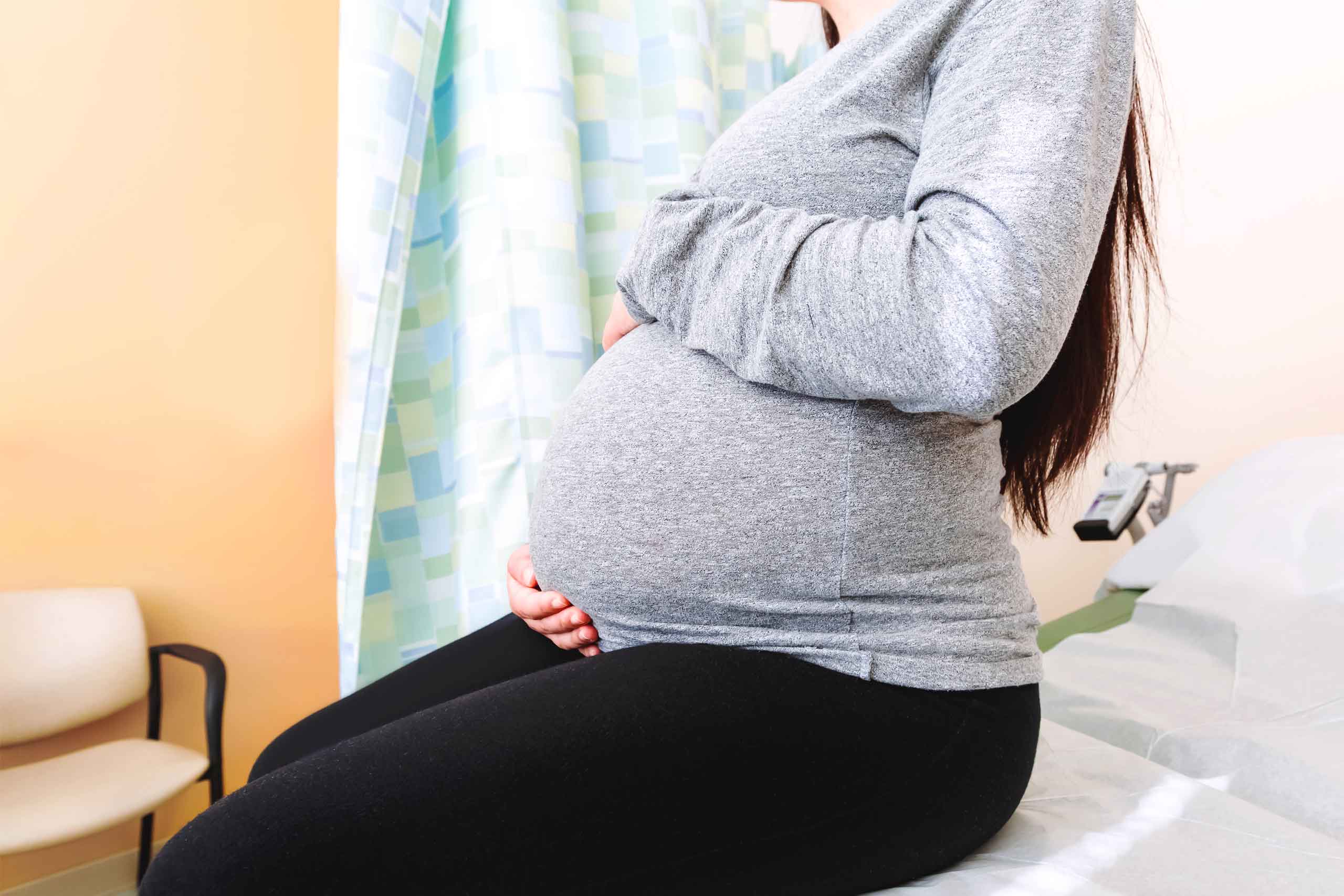 A pregnant woman sits on an exam table and holds her belly