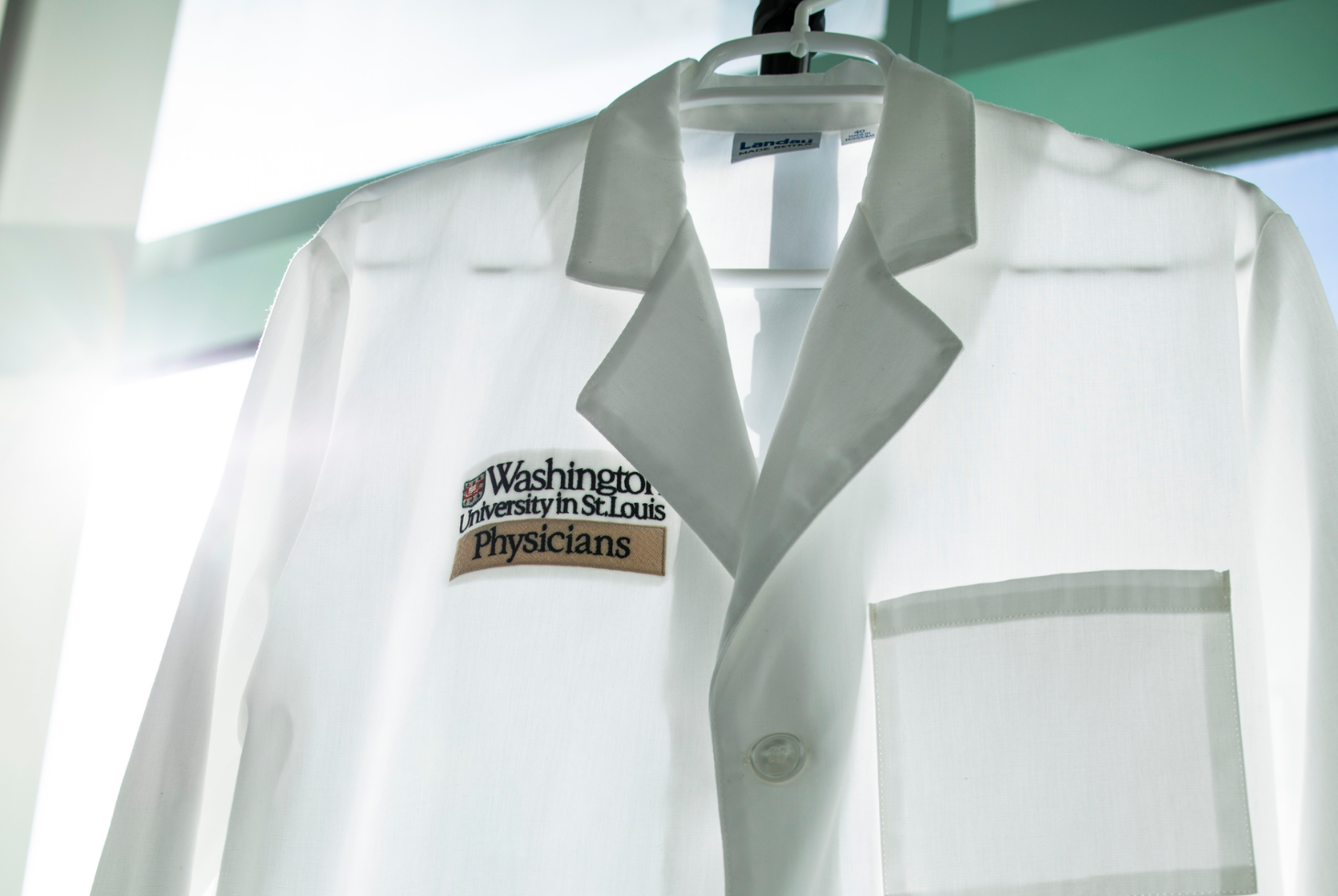 White Washington University Physicians coat hanging in front of a sunny window.