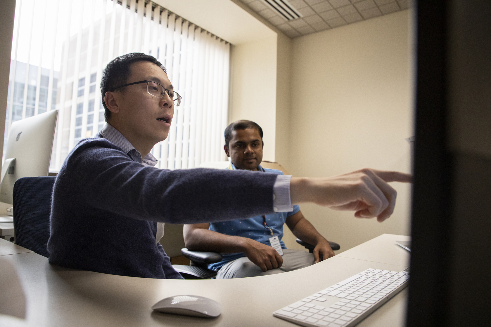 Shuo Wang, PhD, points to a computer screen while working with a member of his lab.