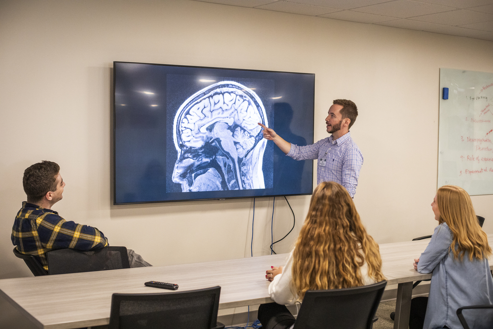 Scott Marek, PhD, points to a brain image on a screen and discusses a project with members of his lab. 