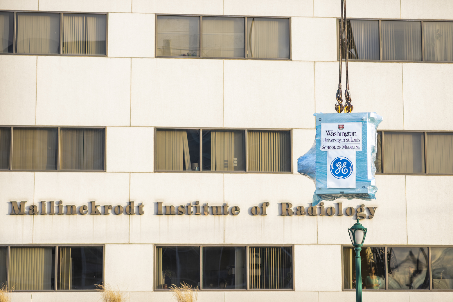A large rectangular box is held up by a crane in front of a building that reads "Mallinckrodt Institute of Radiology"