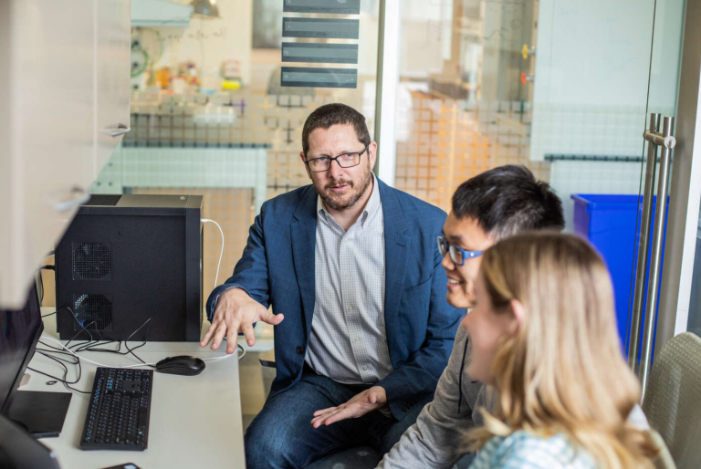 Adam Eggebrecht, PhD, associate professor of radiology, sits center at a computer with two members of his lab.