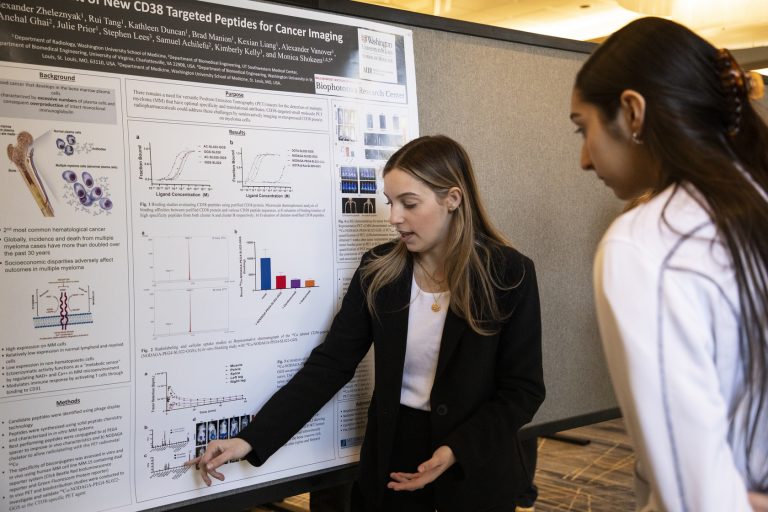 An ISP attendee points to their scientific poster as they speak with another attendee.