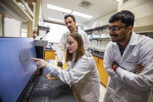 Aisling Chaney, PhD (center), points at a computer screen as she discusses a study with members of her lab.