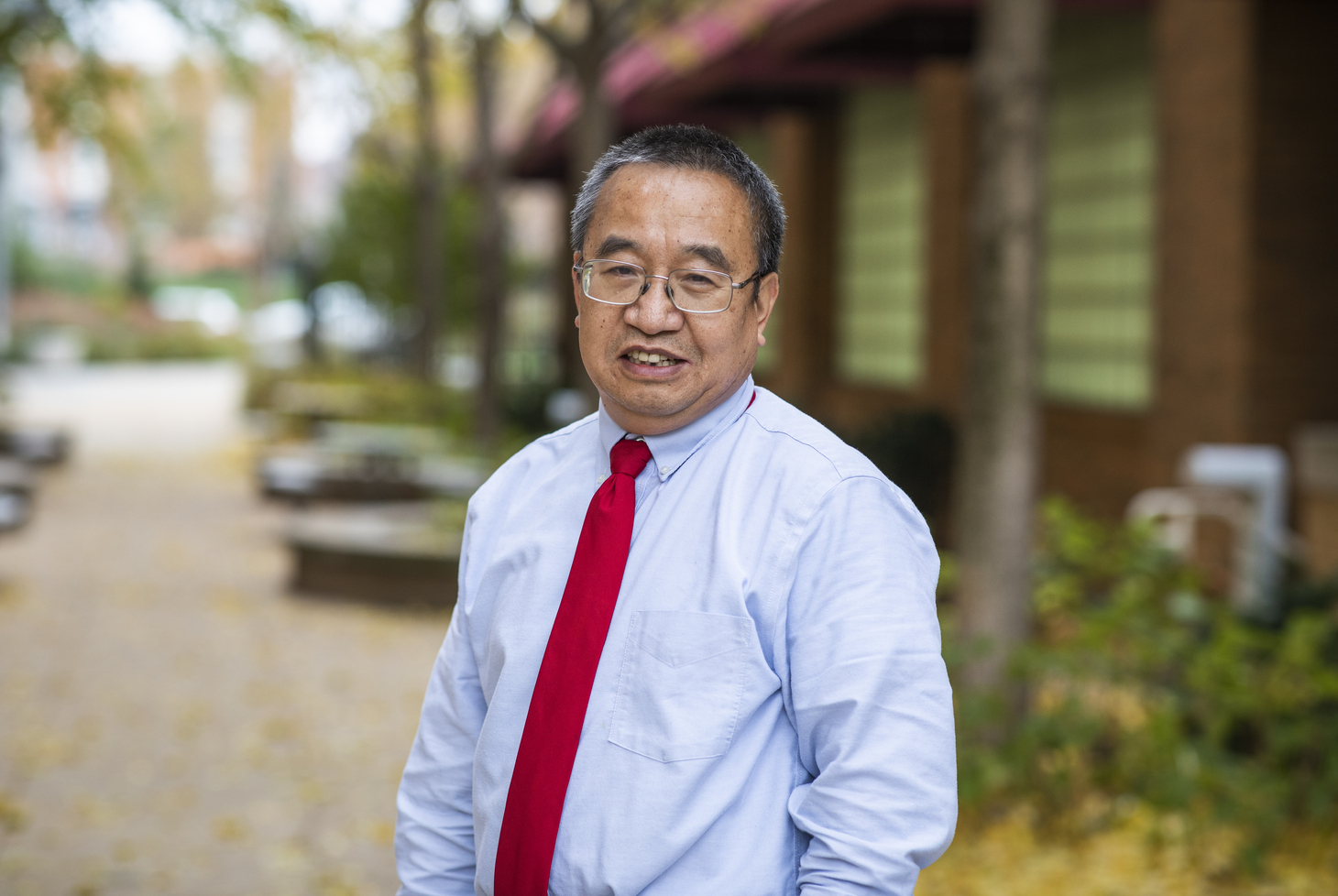 Headshot of Zhude (Will) Tu, PhD, outdoors wearing a blue shirt and red tie.