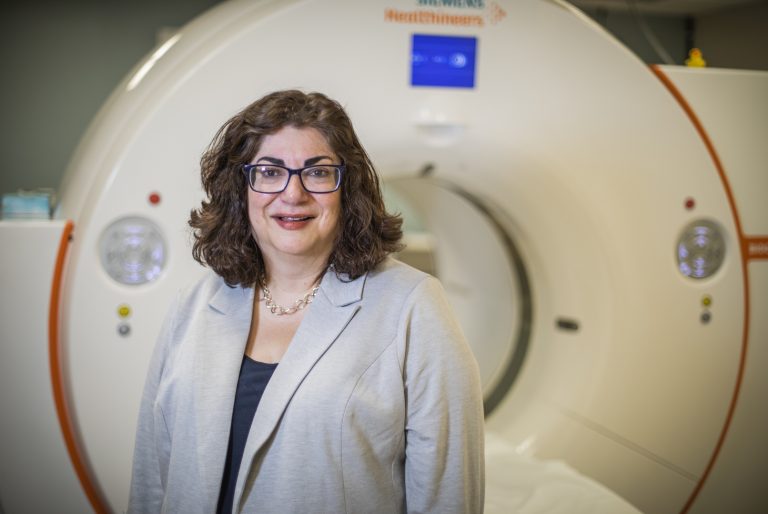 Headshot of Pamela Woodard, MD, standing in a purple blazer in front of a scanner.