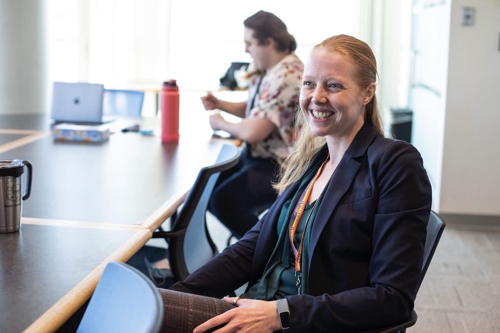 Janine Bijsterbosch, PhD, sitting at a conference table and smiling to someone off camera during a lab meeting.